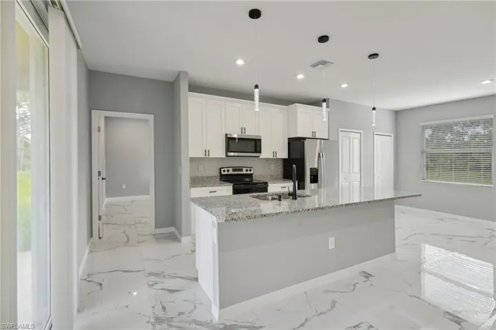 Kitchen with stainless steel appliances, an island with sink, light stone countertops, backsplash, and sink