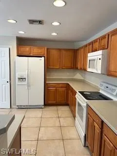Kitchen with brown cabinets, refrigerator, visible vents, and range