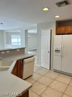 Kitchen featuring brown cabinetry, refrigerator, dishwasher, a sink, and light tile patterned flooring