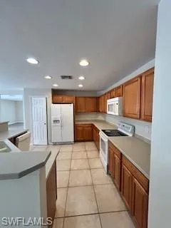 Kitchen featuring brown cabinets, fridge, stove, and light tile patterned flooring
