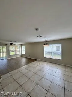 Empty room featuring baseboards, ceiling fan with notable chandelier, and light tile patterned floors