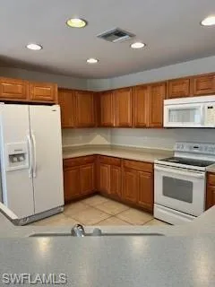 Kitchen featuring visible vents, range, brown cabinets, and fridge