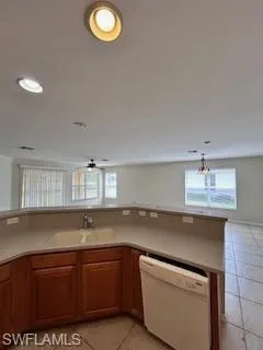 Kitchen featuring light tile patterned flooring, a healthy amount of sunlight, a sink, and dishwasher
