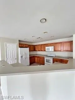 Kitchen featuring brown cabinetry, a peninsula, refrigerator, light countertops, and range