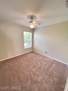 Carpeted empty room with a ceiling fan and baseboards
