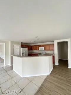 Kitchen with brown cabinetry, a spacious island, refrigerator, baseboards, and light wood-style floors
