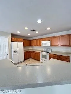Kitchen with brown cabinets, stove, fridge, and visible vents