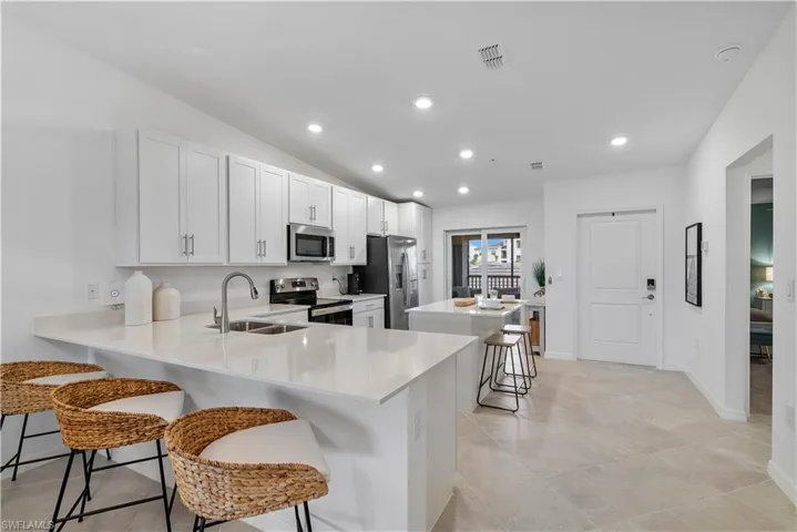 Kitchen featuring kitchen peninsula, sink, appliances with stainless steel finishes, white cabinets, and a kitchen breakfast bar
