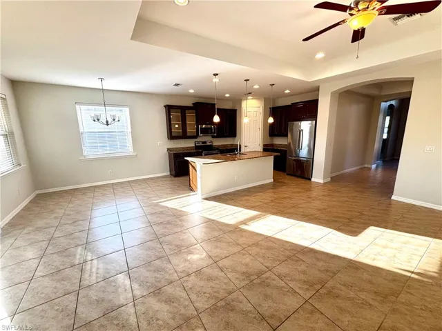 Kitchen featuring open floor plan, glass insert cabinets, arched walkways, a ceiling fan, and a kitchen island with sink