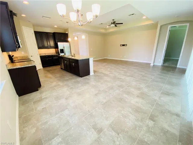 Kitchen featuring ceiling fan, arched walkways, open floor plan, light stone countertops, and a chandelier