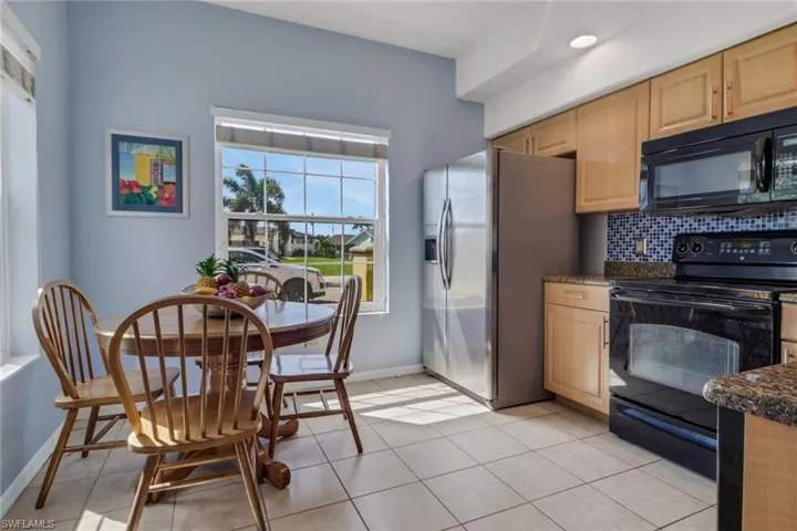 Kitchen with black appliances, light brown cabinets, light tile patterned floors, tasteful backsplash, and stone counters