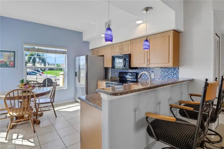 Kitchen featuring light brown cabinets, decorative light fixtures, black appliances, tasteful backsplash, and stone countertops