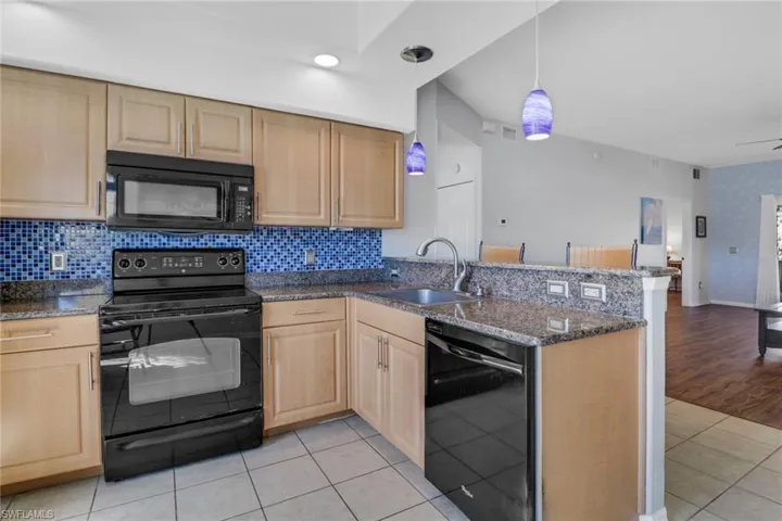 Kitchen with black appliances, stone counters, light tile patterned floors, and open floor plan