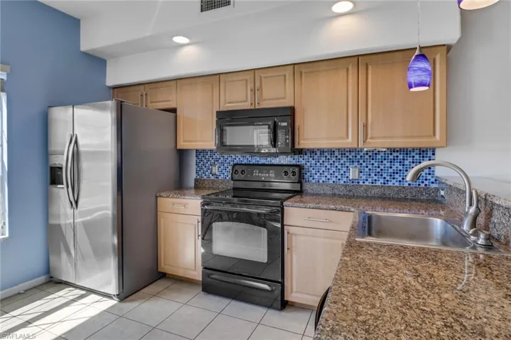 Kitchen featuring black appliances, backsplash, decorative light fixtures, light tile patterned floors, and light brown cabinetry