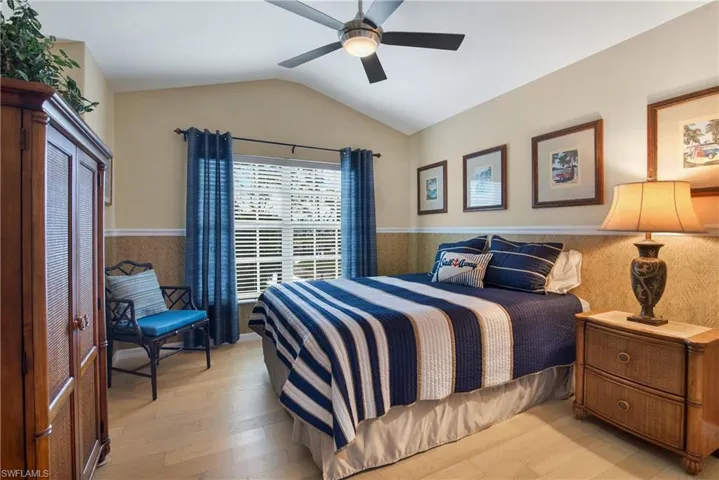 Bedroom with a wainscoted wall, lofted ceiling, light wood finished floors, and ceiling fan