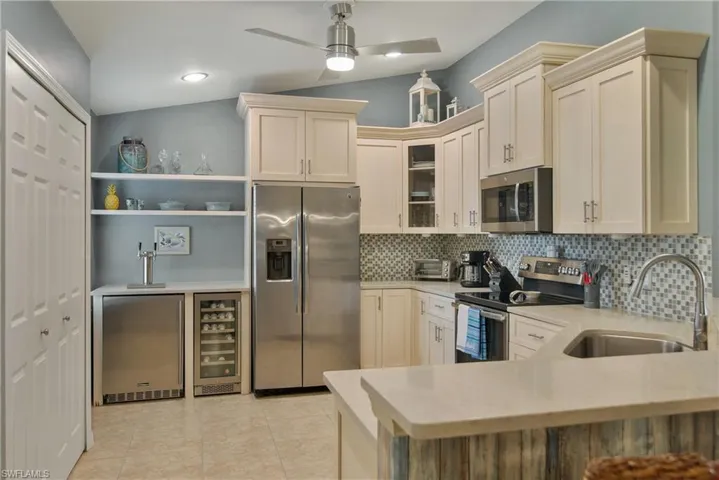 Kitchen featuring stainless steel appliances, wine cooler, light stone counters, lofted ceiling, and backsplash