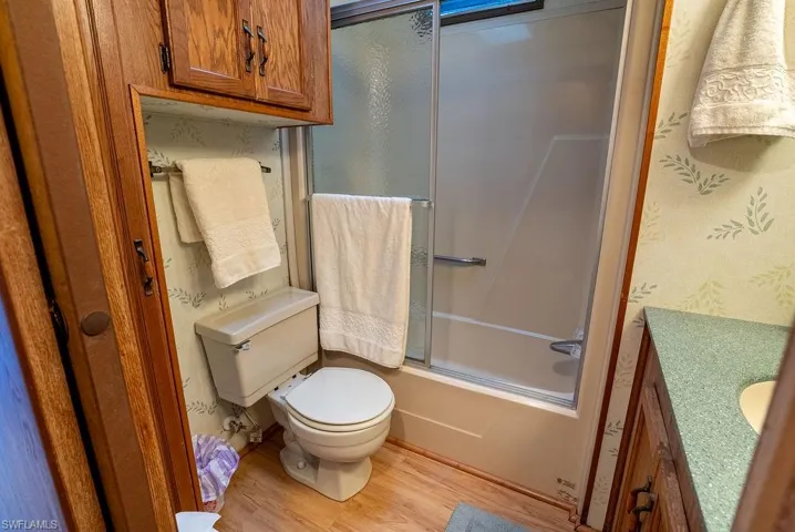 Full bath featuring vanity, light wood-type flooring, shower / bath combination with glass door, and wallpapered walls