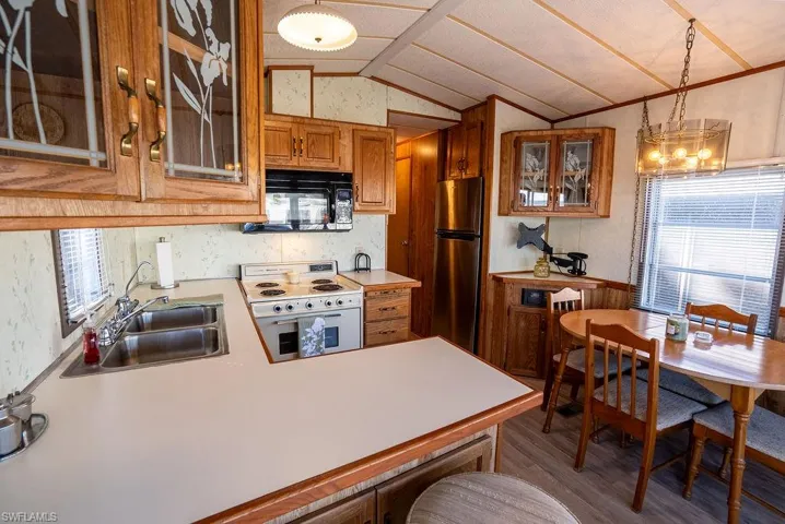 Kitchen with glass insert cabinets, light countertops, brown cabinetry, white range with electric cooktop, and vaulted ceiling