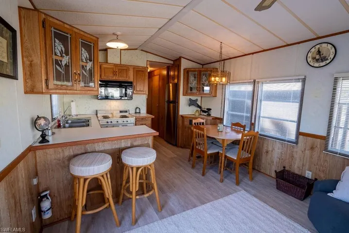 Kitchen featuring wooden walls, a wainscoted wall, a breakfast bar area, glass insert cabinets, and lofted ceiling