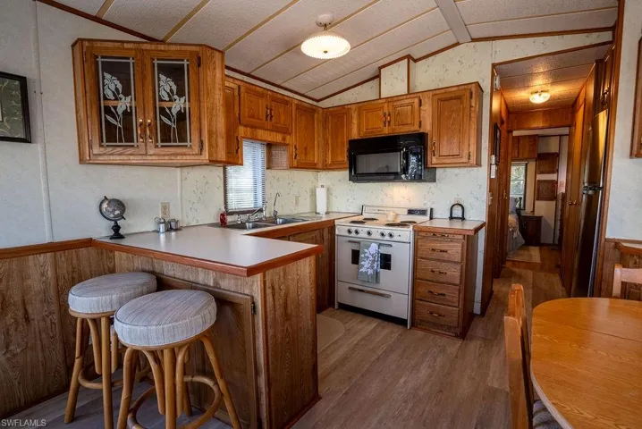 Kitchen with brown cabinetry, electric stove, wooden walls, a kitchen bar, and a peninsula
