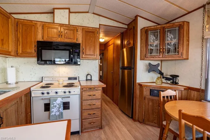 Kitchen featuring electric range, brown cabinets, black microwave, light countertops, and vaulted ceiling