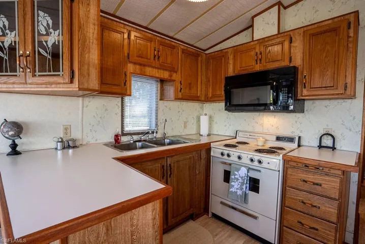 Kitchen featuring brown cabinets, white range with electric cooktop, light countertops, black microwave, and vaulted ceiling
