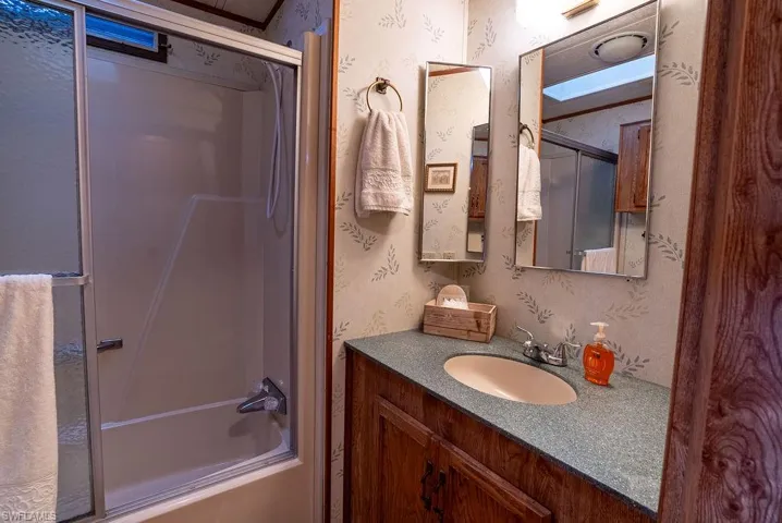 Full bath with wallpapered walls, bath / shower combo with glass door, and vanity