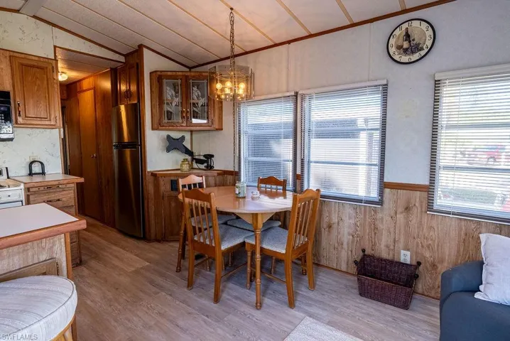 Dining room featuring wooden walls, vaulted ceiling, wainscoting, a chandelier, and light wood finished floors