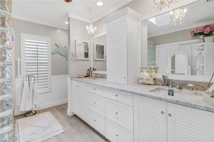 Bathroom with a notable chandelier, dual bowl vanity, and ornamental molding