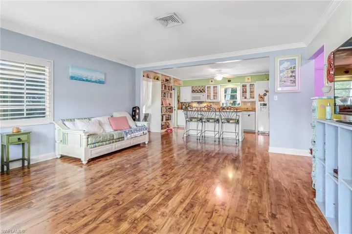 Living room with a wealth of natural light, wood-type flooring, ornamental molding, and ceiling fan