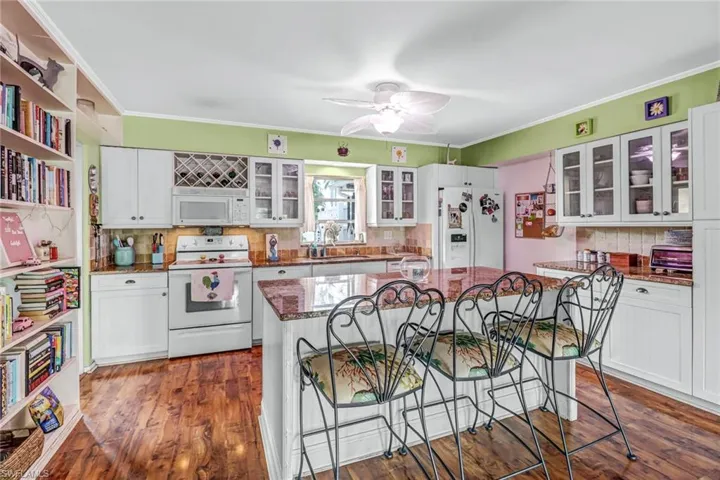 Kitchen with a breakfast bar, white appliances, tasteful backsplash, and dark hardwood / wood-style flooring