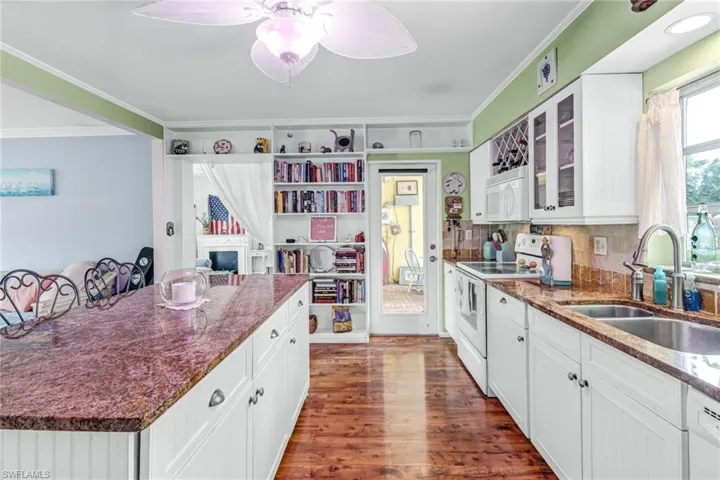Kitchen with crown molding, dark wood-type flooring, white appliances, backsplash, and sink