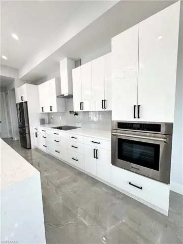 Kitchen with white cabinetry, wall chimney exhaust hood, modern cabinets, stainless steel appliances, and marble finish floor