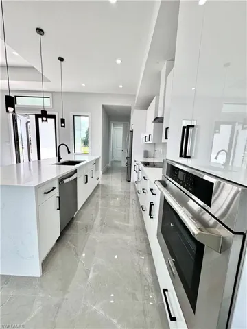 Kitchen with white cabinets, marble finish floor, modern cabinets, appliances with stainless steel finishes, and a sink