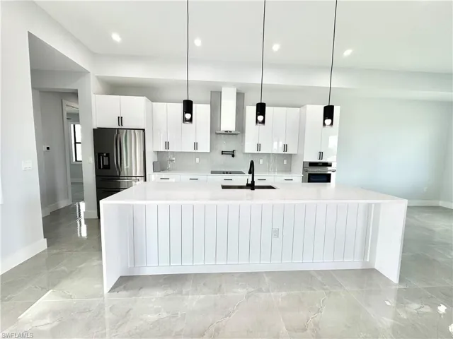 Kitchen featuring light countertops, tasteful backsplash, appliances with stainless steel finishes, a sink, and wall chimney range hood