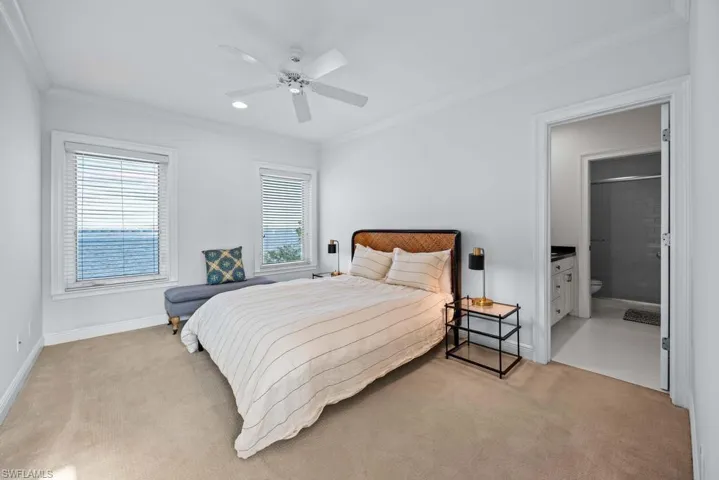 Carpeted bedroom with crown molding, ensuite bath, and ceiling fan