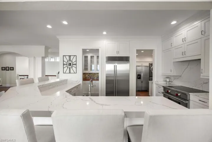 Kitchen with white cabinetry, high end appliances, light stone counters, and a kitchen bar