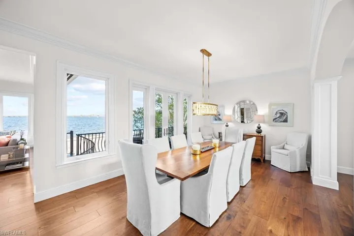 Dining space featuring a water view, ornamental molding, dark hardwood / wood-style floors, and decorative columns