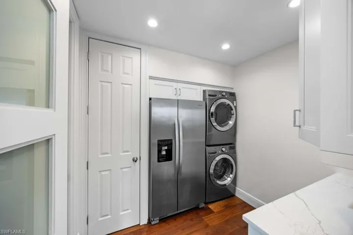 Laundry room with stacked washer and dryer and dark hardwood / wood-style flooring