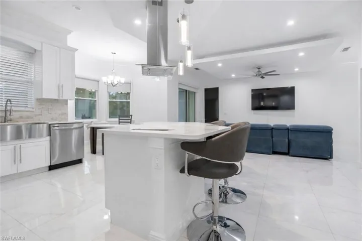 Kitchen featuring white cabinetry, a kitchen island, dishwasher, light stone countertops, and lofted ceiling with beams