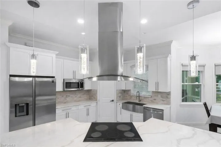 Kitchen featuring island range hood, stainless steel appliances, crown molding, white cabinets, and hanging light fixtures
