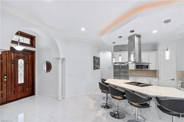 Kitchen with arched walkways, decorative light fixtures, white cabinetry, and ornamental molding
