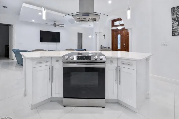 Kitchen featuring stainless steel electric stove, open floor plan, island range hood, and white cabinets