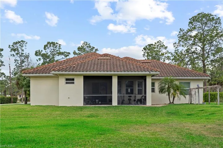 Back of property with a yard, stucco siding, a tile roof, and a sunroom