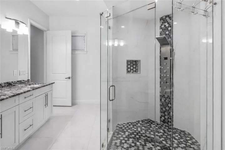 Full bathroom with double vanity and a marble finish shower