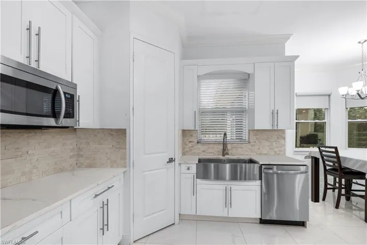 Kitchen with stainless steel appliances, white cabinets, ornamental molding, light stone counters, and light marble finish floors