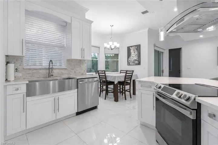 Kitchen with stainless steel appliances, exhaust hood, light stone counters, crown molding, and white cabinetry