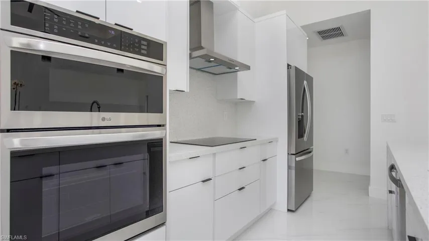 Kitchen with wall chimney range hood, appliances with stainless steel finishes, light marble finish floors, modern cabinets, and white cabinets