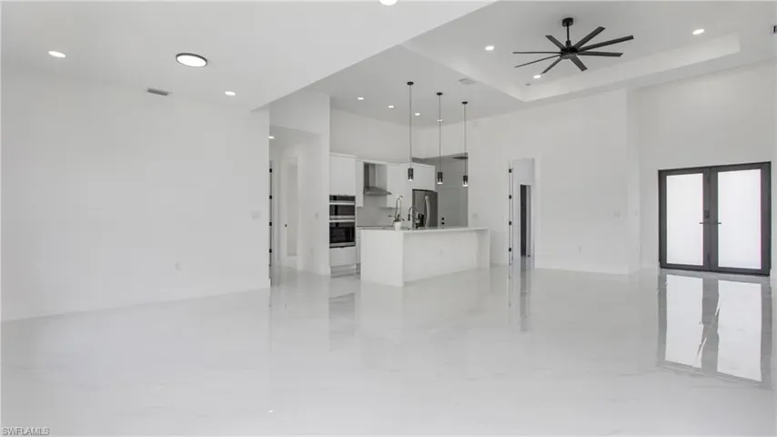 Unfurnished living room featuring a high ceiling, recessed lighting, light marble finish floors, ceiling fan, and french doors