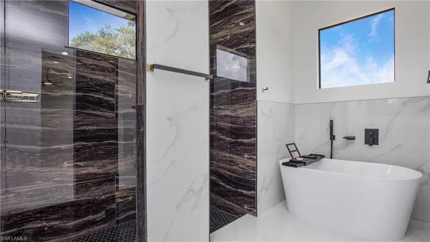 Full bathroom featuring tile walls, a freestanding bath, marble tiled flooring, a marble finish shower, and healthy amount of natural light
